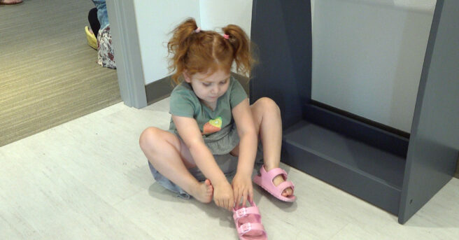 A girl sitting on the floor putting her shoes on.