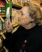 older woman using magnifier to examine products on grocery store shelf