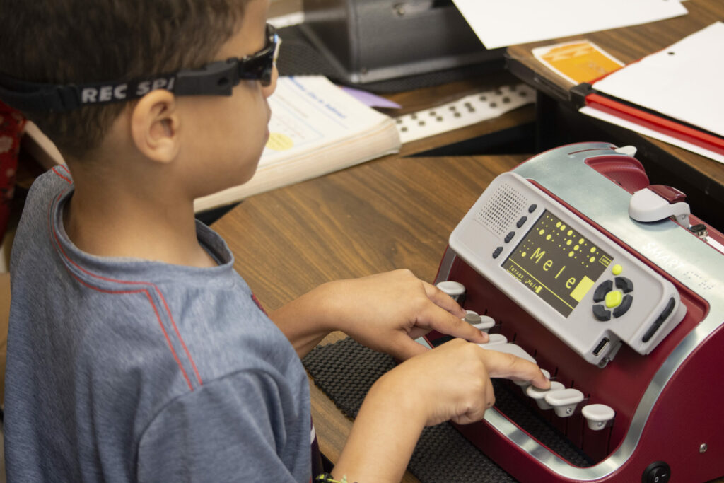 A young boy wearing glasses with a smart brailer.