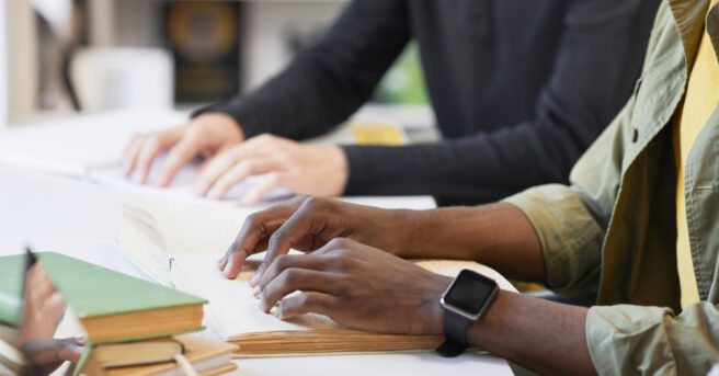 Two people using their hands to read braille