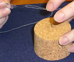 Remove the wire loop from the eye of the needle by grasping the metal disk or handle and pulling it back out until the end of the thread is free from the wire loop. Keep pulling until the thread is completely free.
