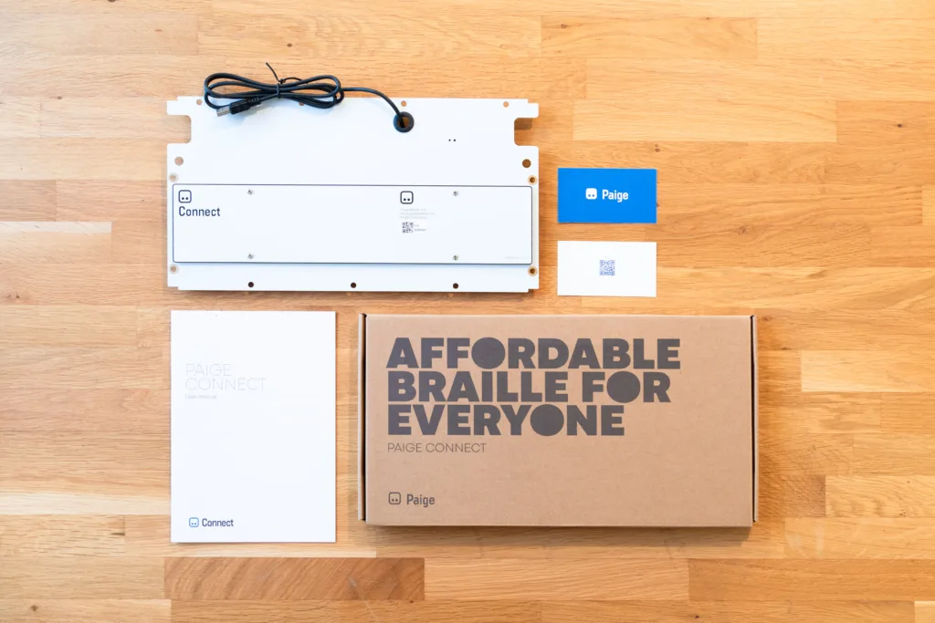 Bottom of Paige Connect Device, brochure, box and information card sitting on a table.