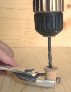 A pair of pliers holding a wooden spool with drill bit inserted through hole in spool, used as a drill guide