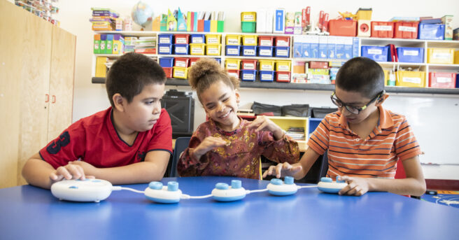 Three students sitting at at classroom table working with the code jumper.