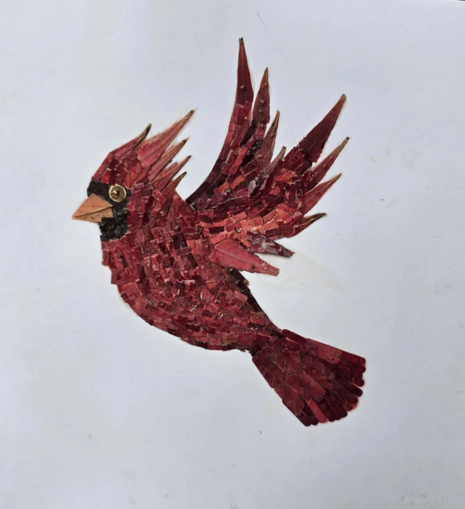 red leaves cut into various shapes are glued to paper to depict a cardinal in flight 