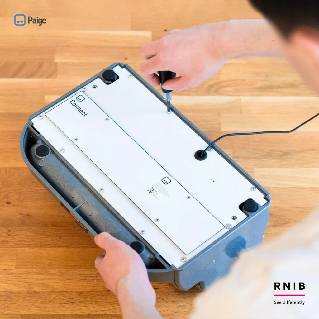 An adult installing the Paige Connect Device to a traditional braille writer.