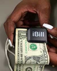 a woman's hands feeding a one dollar bill into the iBill Money Identifier