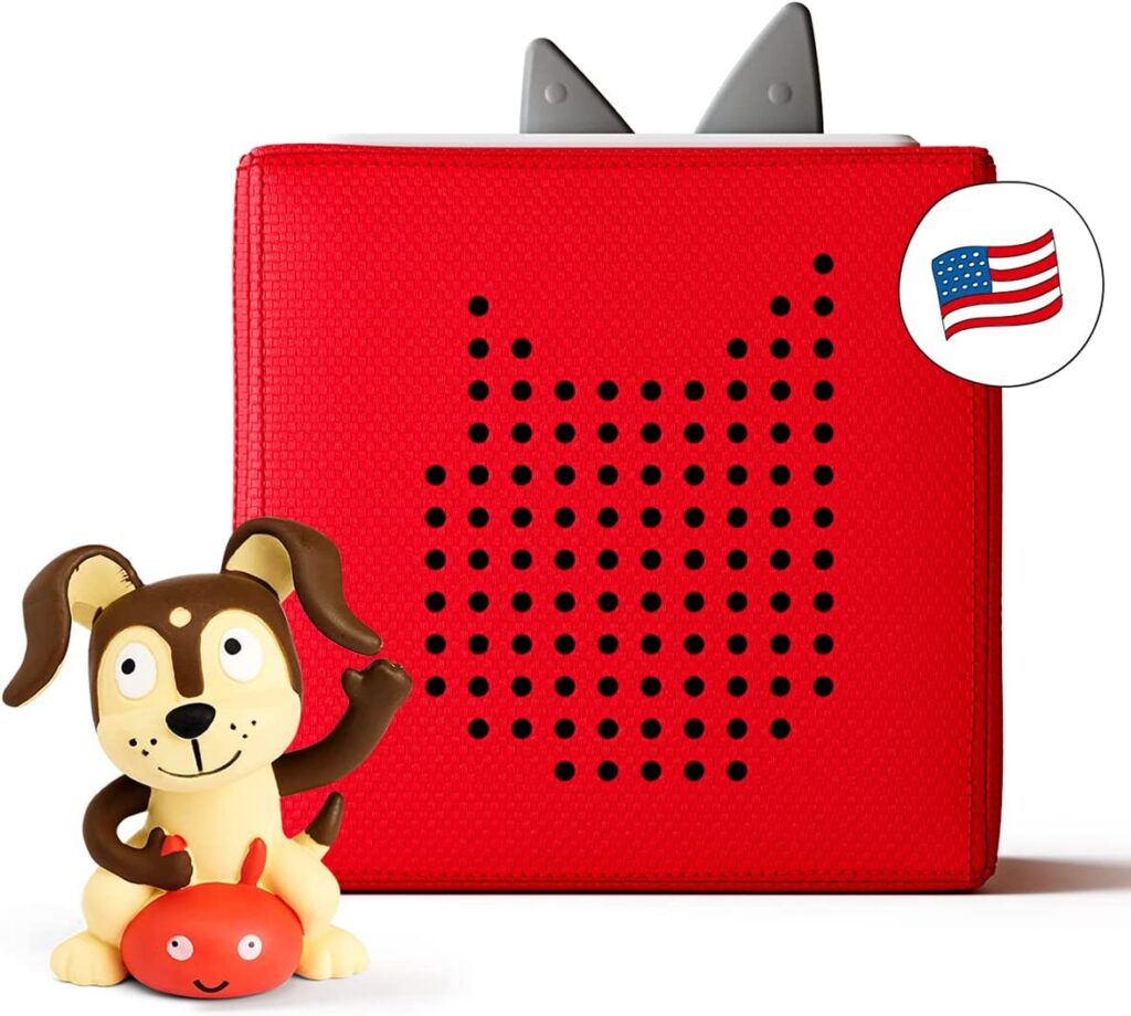 A red Toniebox with grey ears with a  dog figurine in front of it.  