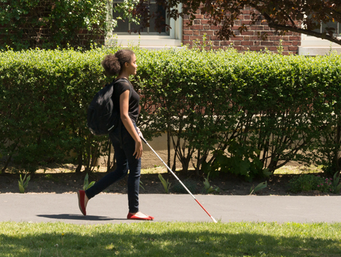 Teenage girl walking with cane on sunny day
