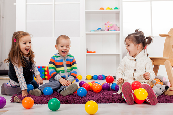 Three small children sitting on the floor playing with brightly colored balls