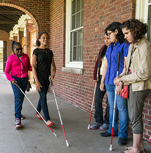 Students with white canes hanging out and walking in an outside school hallway.