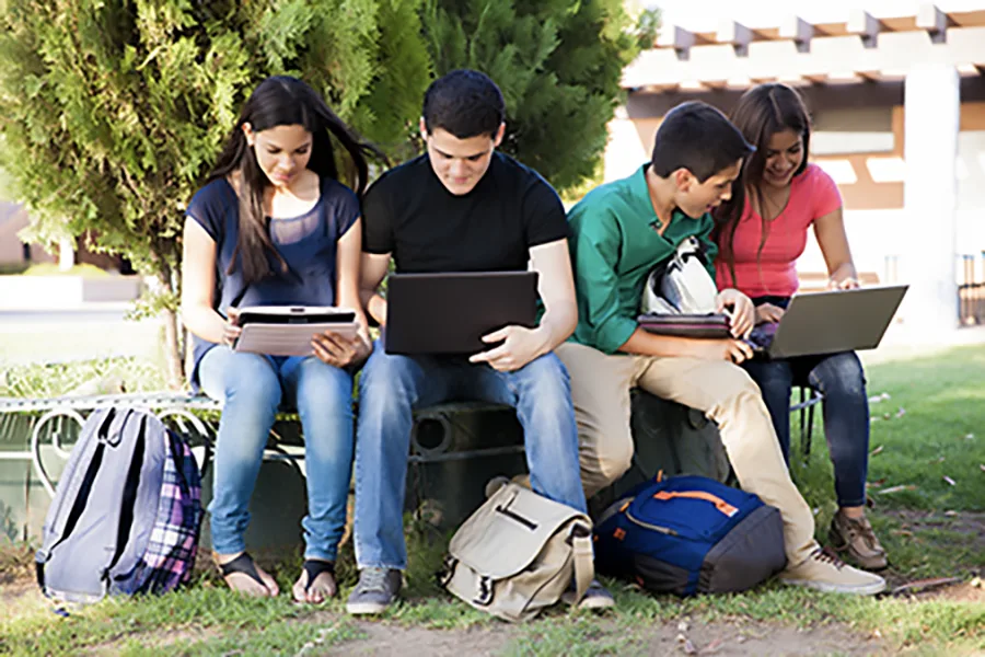 group of students sitting outside working on their laptops.
