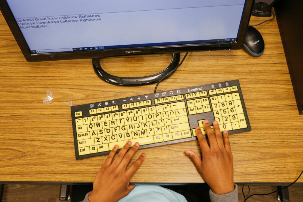 Student's fingers on a yellow keyboard. with a computer screen.