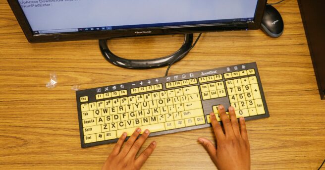Student's fingers on a yellow keyboard. with a computer screen.