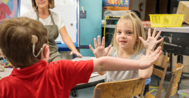 Two preschoolers sitting at a table giving high fives.