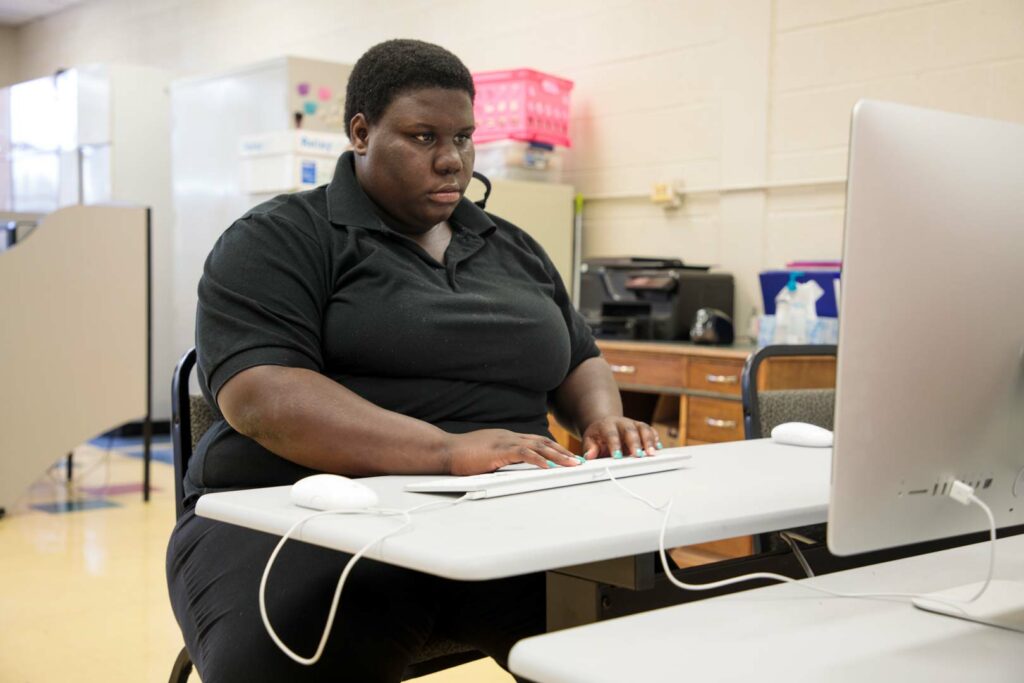 A young adult sitting at a table working on a computer typing.