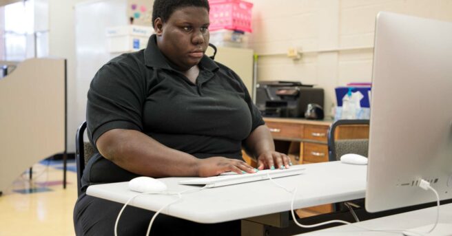 A young adult sitting at a table working on a computer typing.