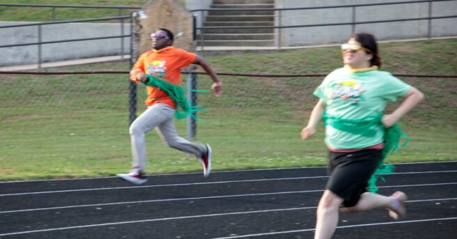 Two students wearing sunglasses running on a track.