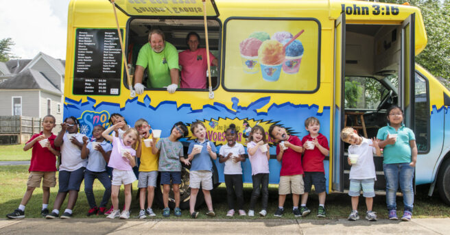 A group of preschoolers standing against an ice cream truck enjoying ice cream.