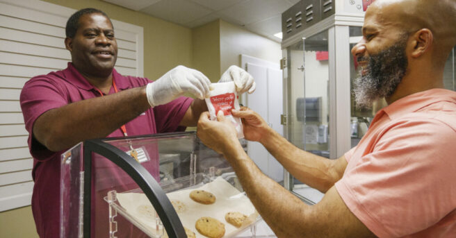 A man handing a cookie to a customer over the counter.