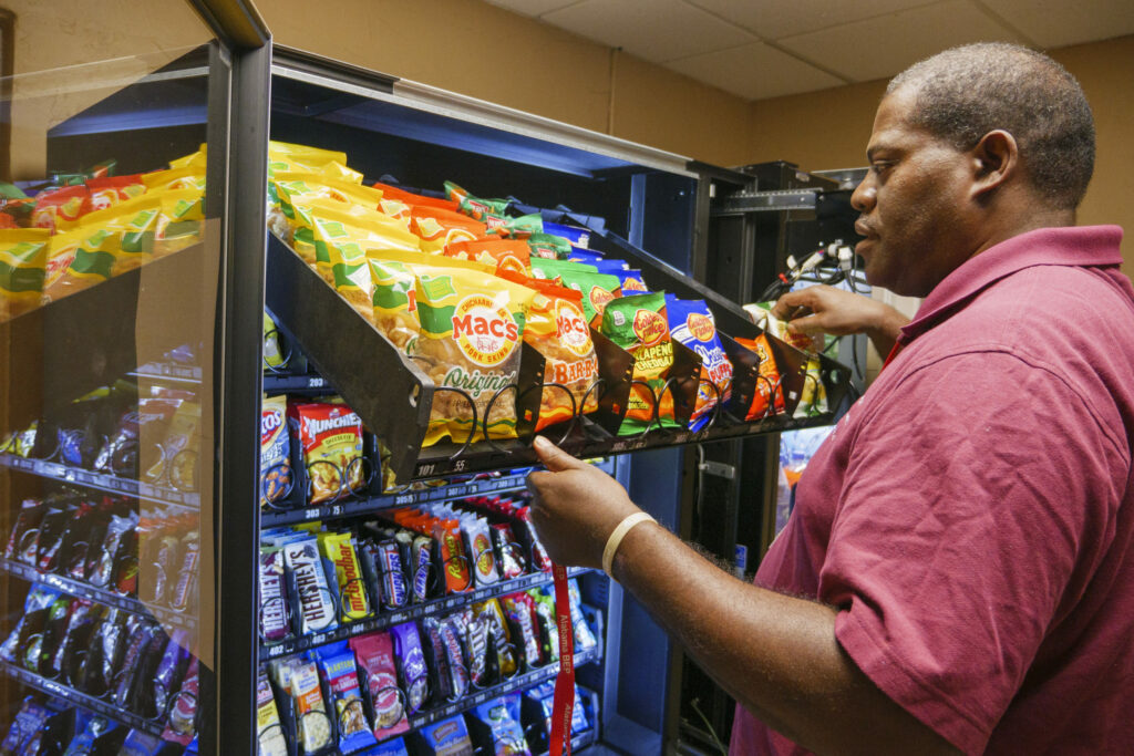 Man loading a vending machine with snacks.