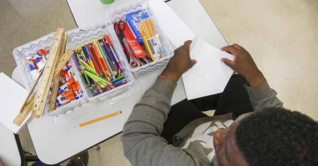 A student with supplies on his des organized into bins.