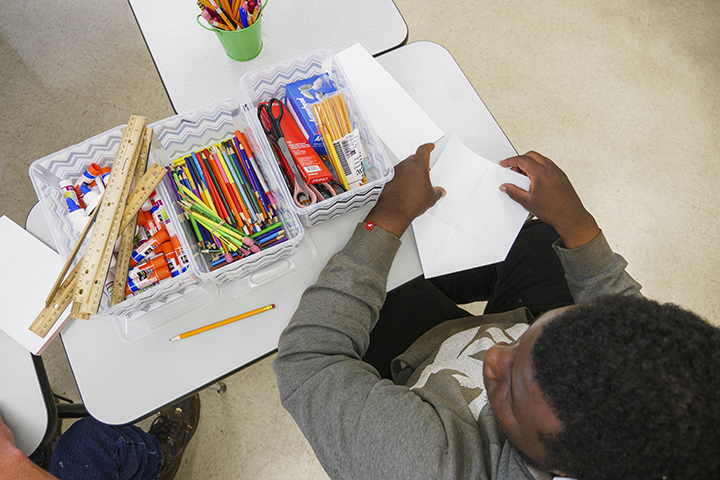 A student with supplies on his des organized into bins.