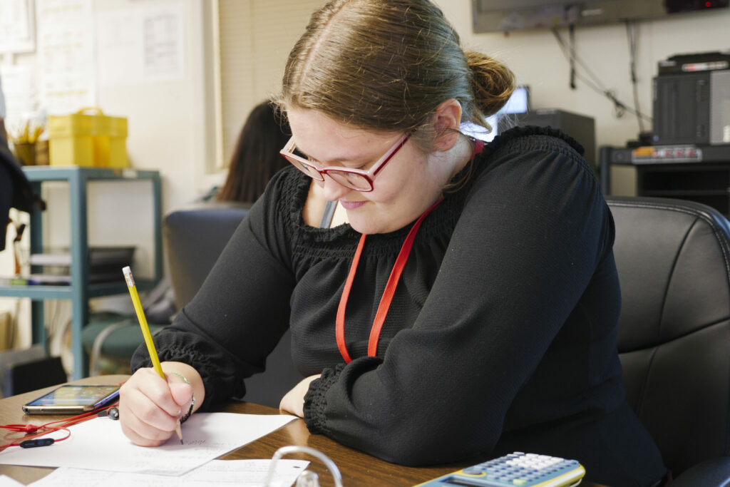 Girl with glasses sitting at a desk writing