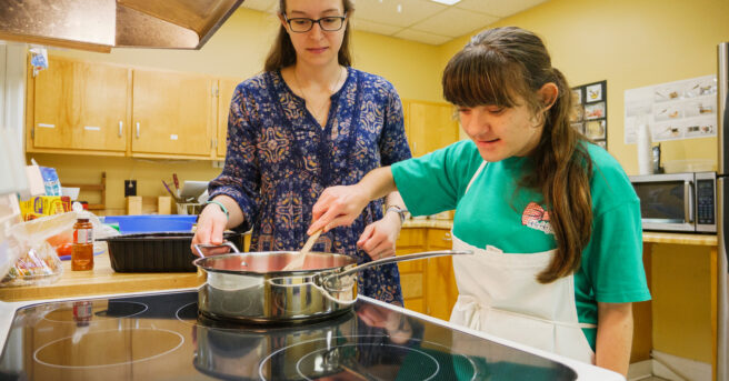 A teen learning how to use a stove for cooking with a parent.