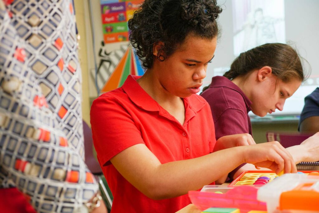 Two students working with a teacher standing next to them.