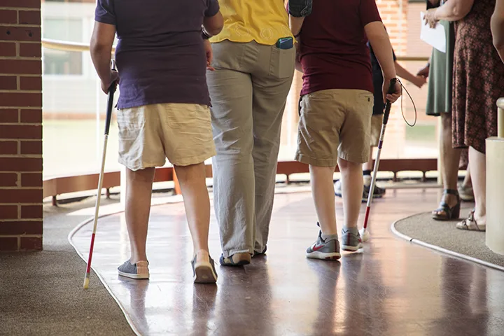 2 students with canes and an adult walking in hallway