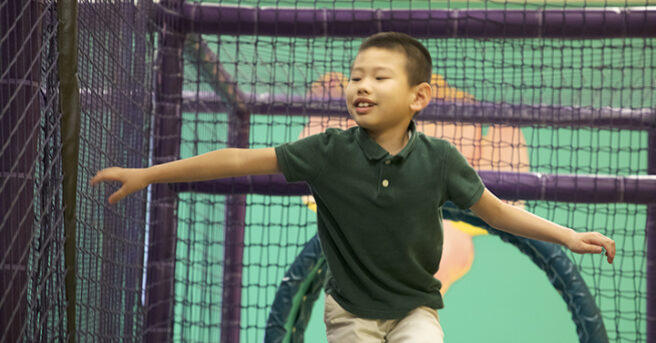 A boy walking through an indoor obstacle course. His arms are out.