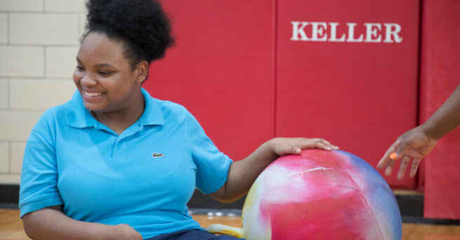 A teen sitting on the gym floor engaging with a large colorful ball.