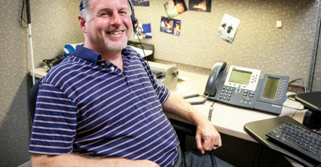 Alan smiling wearing headset with phone and laptop