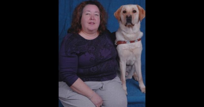 Person sitting for a professional photo with a dog guide in harness.