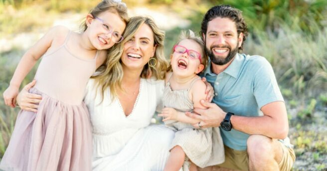 An image of the Spirito family outdoors, Mom and Dad with their arms around two young, smiling girls wearing pink glasses.