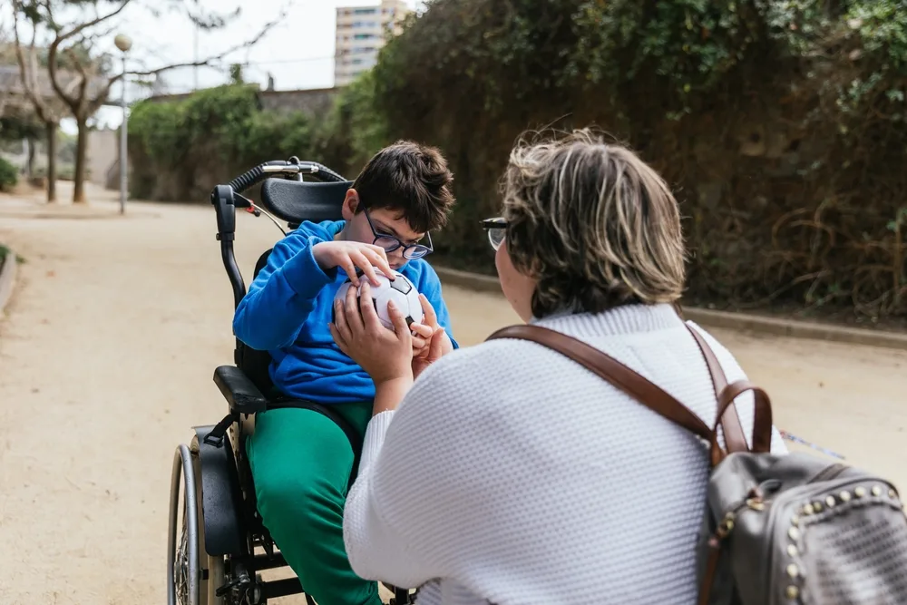 child in a wheelchair explores a soccer ball with an attentive adult 