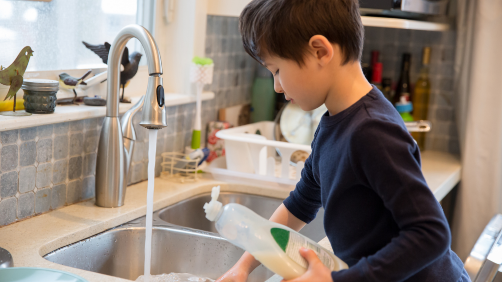 A child at a sink washing dishes.