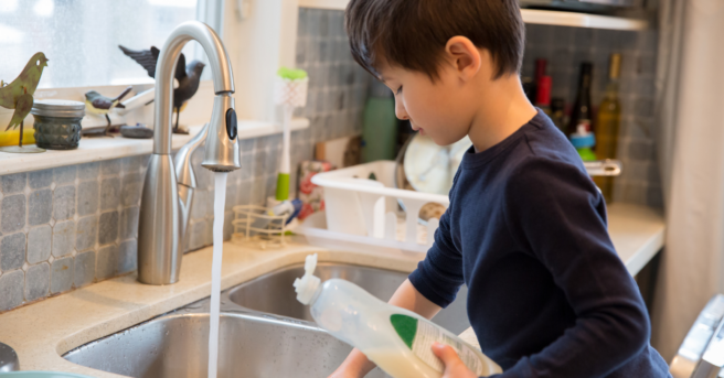A child at a sink washing dishes.