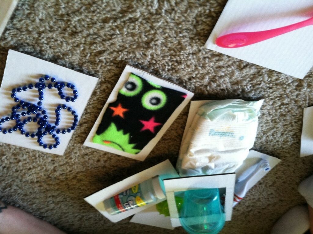 Photo of object attached to communication cards. Cards for Diaper, beads, bottle, toothbrush, cup, spoon and a piece of blanket flannel.