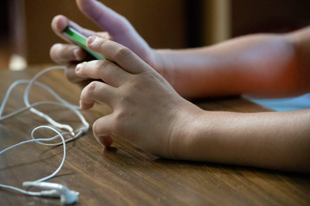 A child's hands holding a phone with earbuds plugged in.