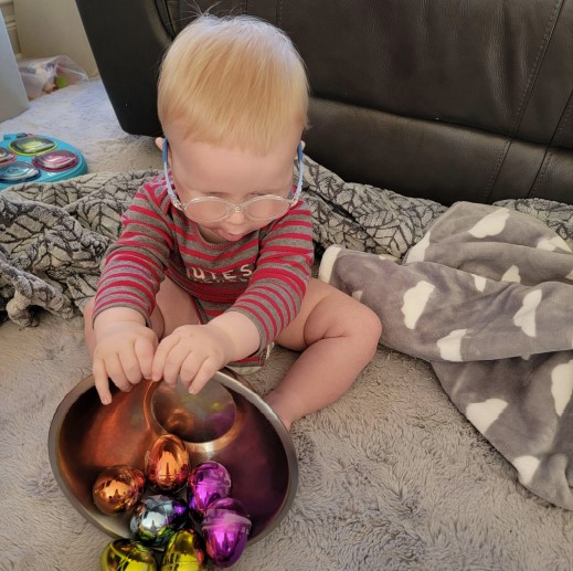 Dominic sitting on the floor holding a bowl filled with various egg shakers.