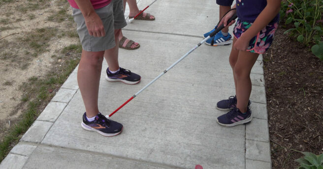 Two adults facing two children holding canes outside on a sidewalk.