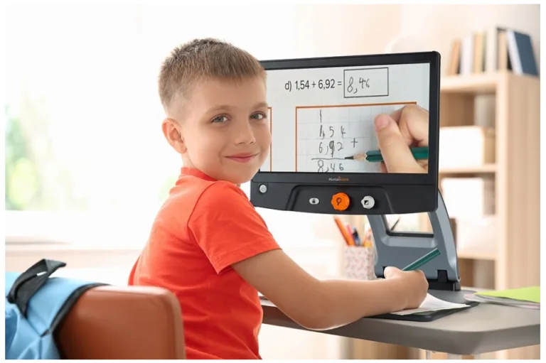 "Young boy sitting at desk using magnifying reader to do schoolwork."
