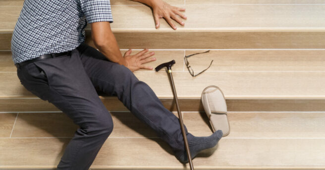 Older man lying on steps with cane, glasses and slipper beside him where he fell