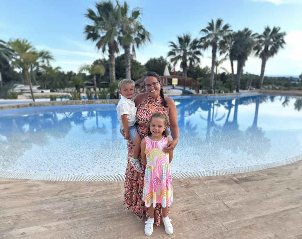 Adult wears glasses and poses with two children in front of a swimming pool