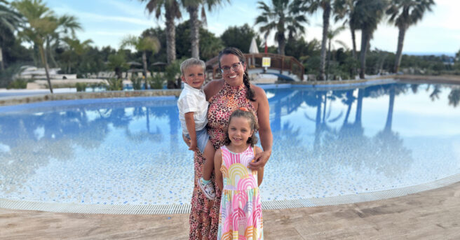 Adult wears glasses and poses with two children in front of a swimming pool