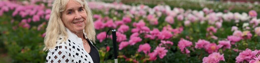 image of Gena holding cane in front of a field of pink flowers