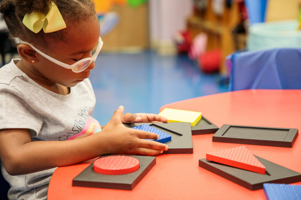 Young girl sitting at table playing with circles and squares fitting them into spaces.