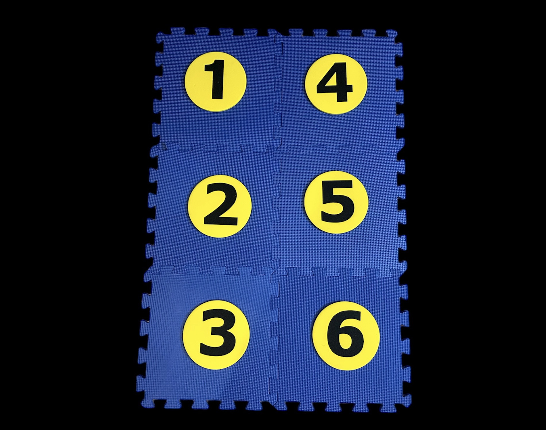 large floor mat, a Hop-A-Dot, representing a braille cell. It has six blue squares made of foam that interlock. Inside each square is one large removable yellow foam circle with a number 1-6 on it.